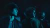 An image of three young men standing, bathed in blue light